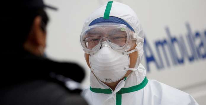 FILE PHOTO: A hospital staff member in protective garments talks to a police officer at a checkpoint to the Hubei province exclusion zone at the Jiujiang Yangtze River Bridge in Jiujiang